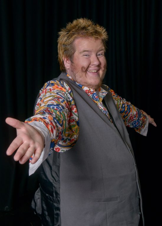 Narrator Matt with big smile with drawn on curled moustache wearing bright shirt and waistcoat