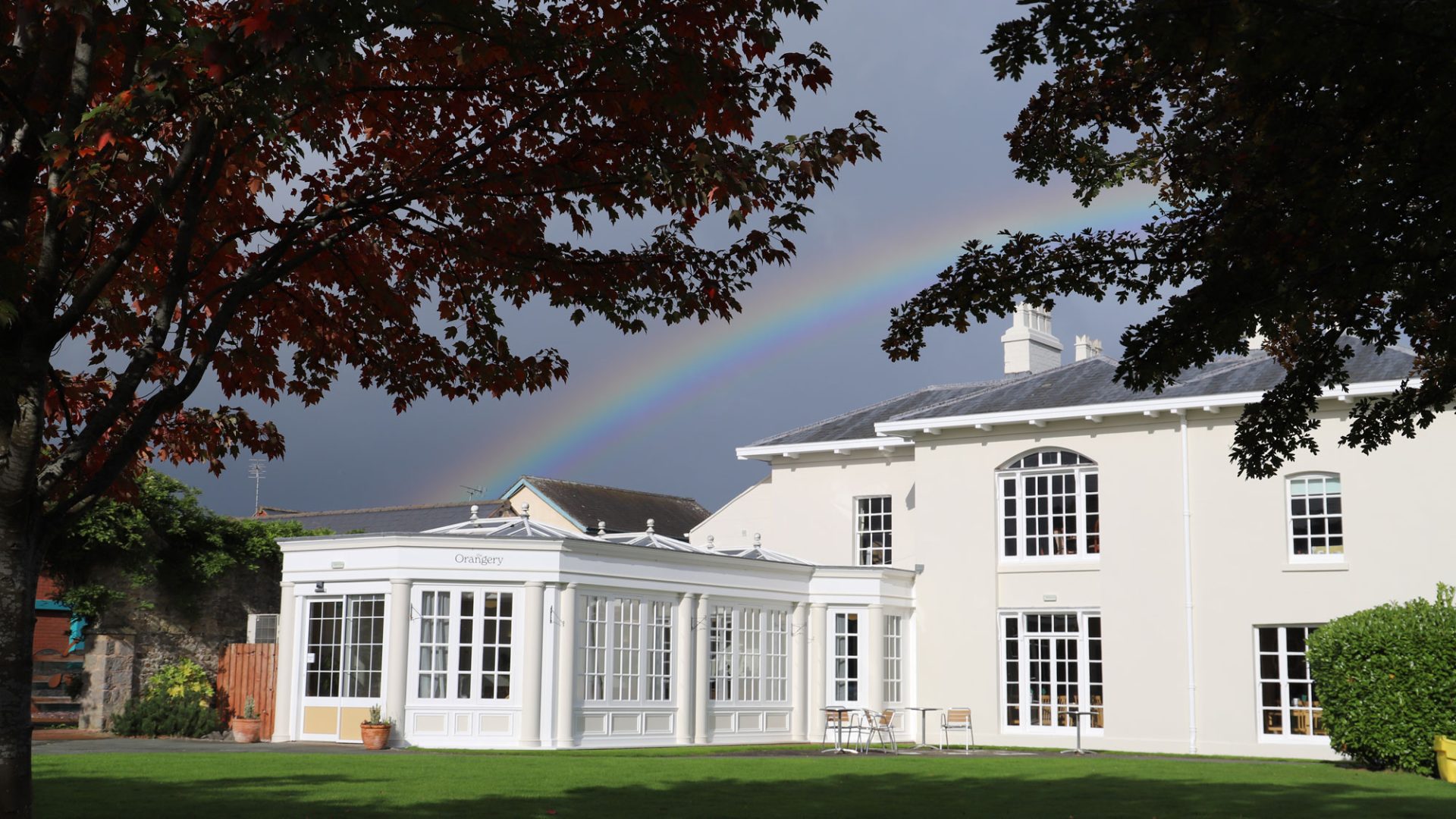 view through the tree of the orangery restaurant, with a rainbow in the grey sky above
