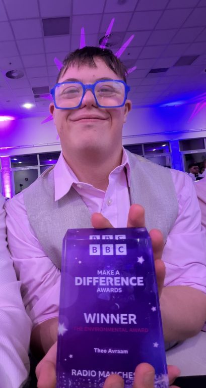 Close up photo or Theo wearing blue glasses and holding up his Make a Difference winners award.