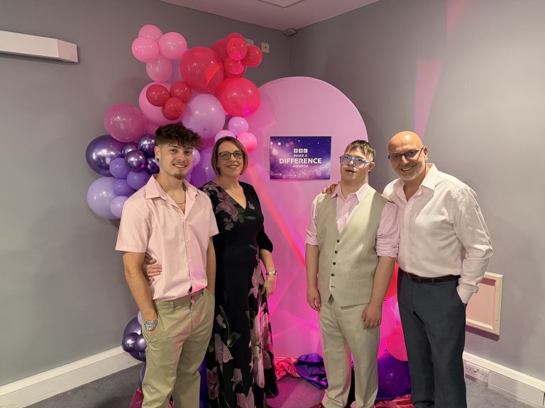 Four family members - Theo with mum, dad and brother - dressed smartly in pink shirts and dress, in front of pink and purple balloons and Make ad Difference logo.
