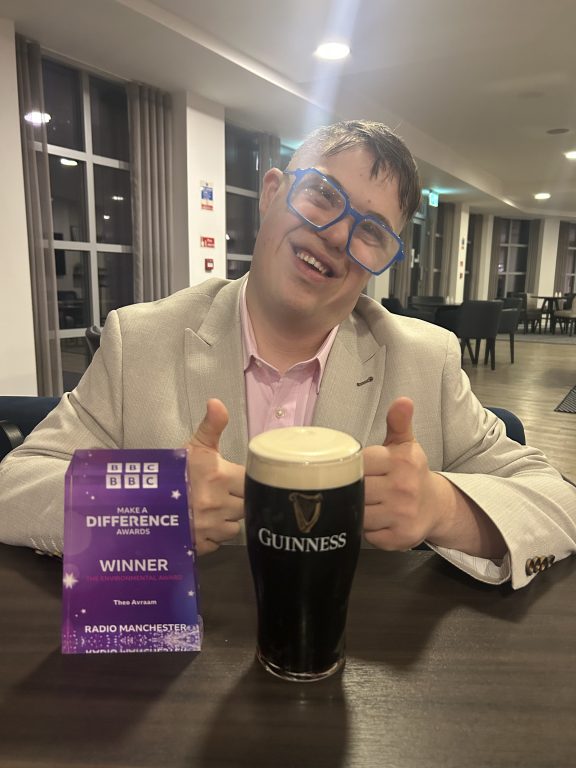 Young man dressed smartly sat at a table with his Make a Difference trophy and a full pint of Guinness.