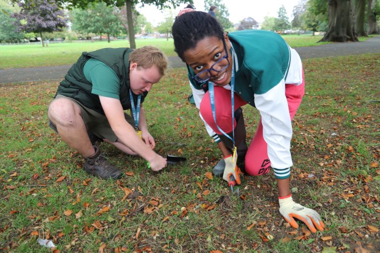 a male and female student using trowels to dig holes to plant bulbs in a park.