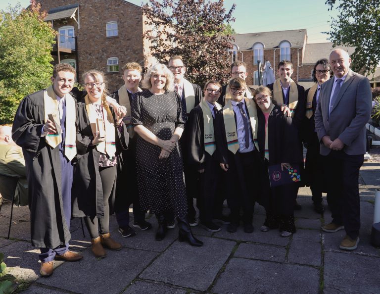 large group of graduates wearing gowns and sashes out in the sun with principal Meryl and chair of governors Jamie.